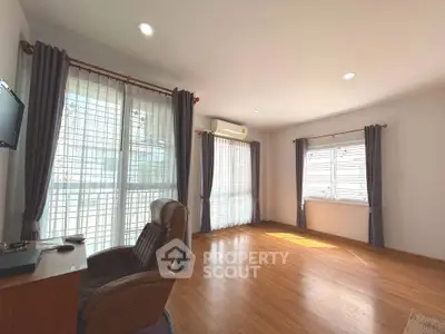 Spacious and bright living room with wooden flooring and large windows in modern apartment.