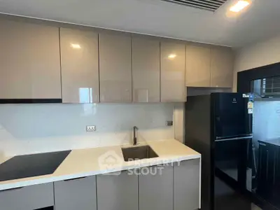Modern kitchen with sleek cabinetry and black fridge in a contemporary apartment.
