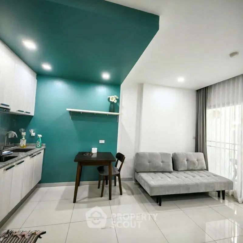 Modern open-layout kitchen and living room with teal accent wall and sleek furniture.