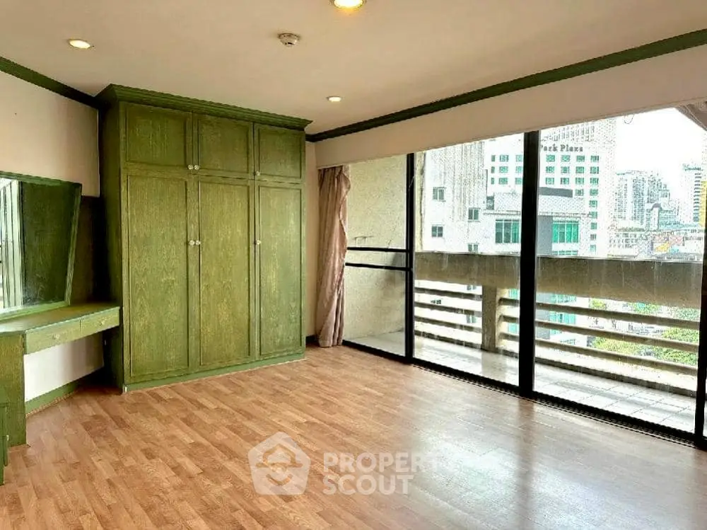 Spacious bedroom with large windows and city view, featuring wooden flooring and built-in wardrobe.