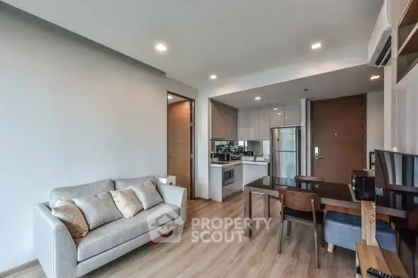 Modern open-layout living room with kitchen and dining area, featuring sleek furniture and wooden flooring.