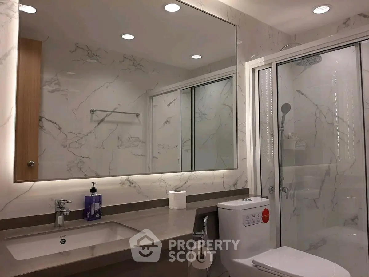 Luxurious bathroom with elegant marble walls and modern fixtures, featuring a spacious shower and sleek vanity.