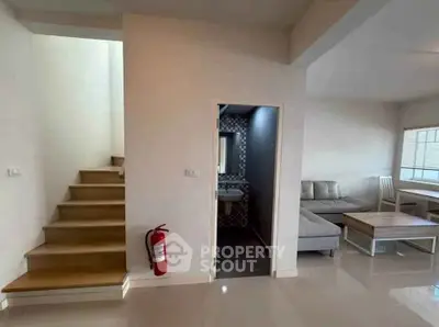 Modern living room with staircase and open layout, featuring sleek furniture and a cozy atmosphere.