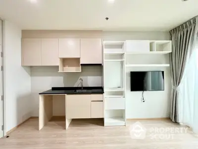 Modern studio apartment with sleek kitchen featuring built-in appliances and ample storage, complemented by light wood flooring and neutral tones.