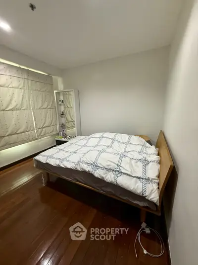 Cozy bedroom with wooden flooring and modern decor in a well-lit apartment.