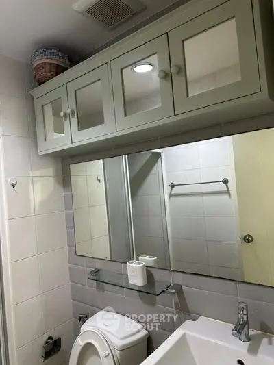 Modern bathroom with sleek cabinetry and mirror, featuring a compact design and neutral tones.