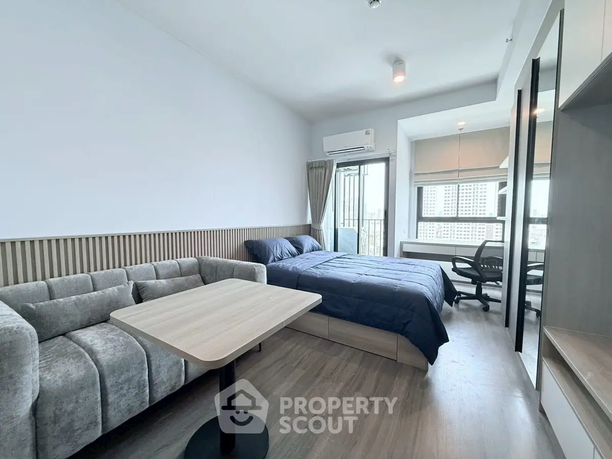 Modern studio apartment with cozy living area and city view balcony.