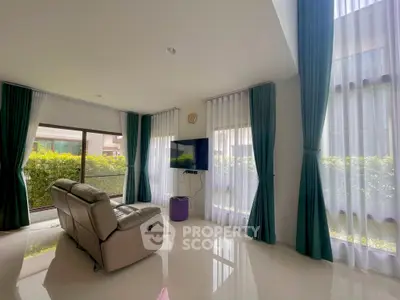 Spacious living room with modern decor and large windows offering natural light and garden view.