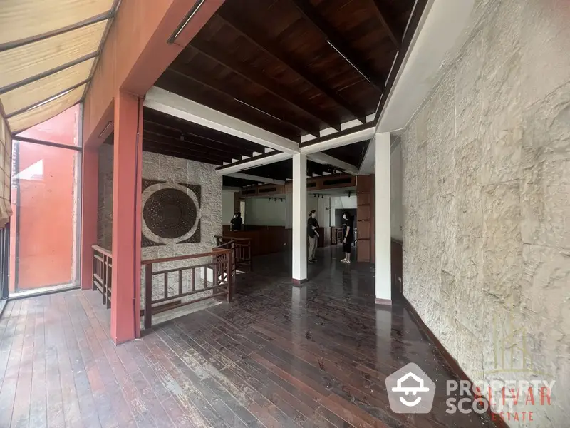 Expansive covered balcony with polished wooden floors and rustic stone walls, offering a seamless indoor-outdoor living experience in a serene setting.