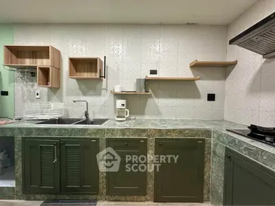 Modern kitchen with green cabinets and open shelving, featuring a sleek countertop and built-in stove.