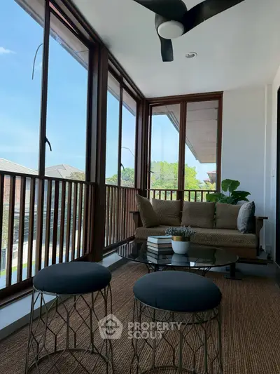 Charming enclosed balcony with cozy seating and large windows offering a serene view.