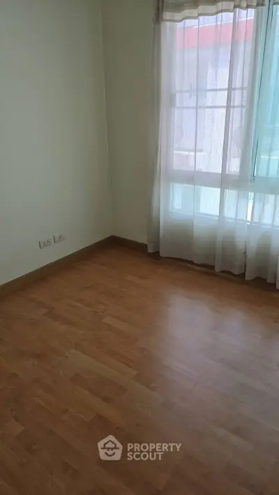 Spacious empty room with wooden flooring and large window, perfect for customization.