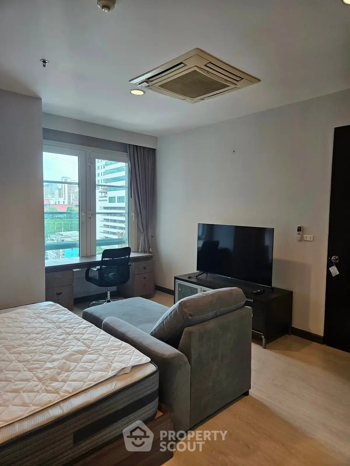 Modern studio apartment with large window and city view, featuring a cozy sofa and flat-screen TV.