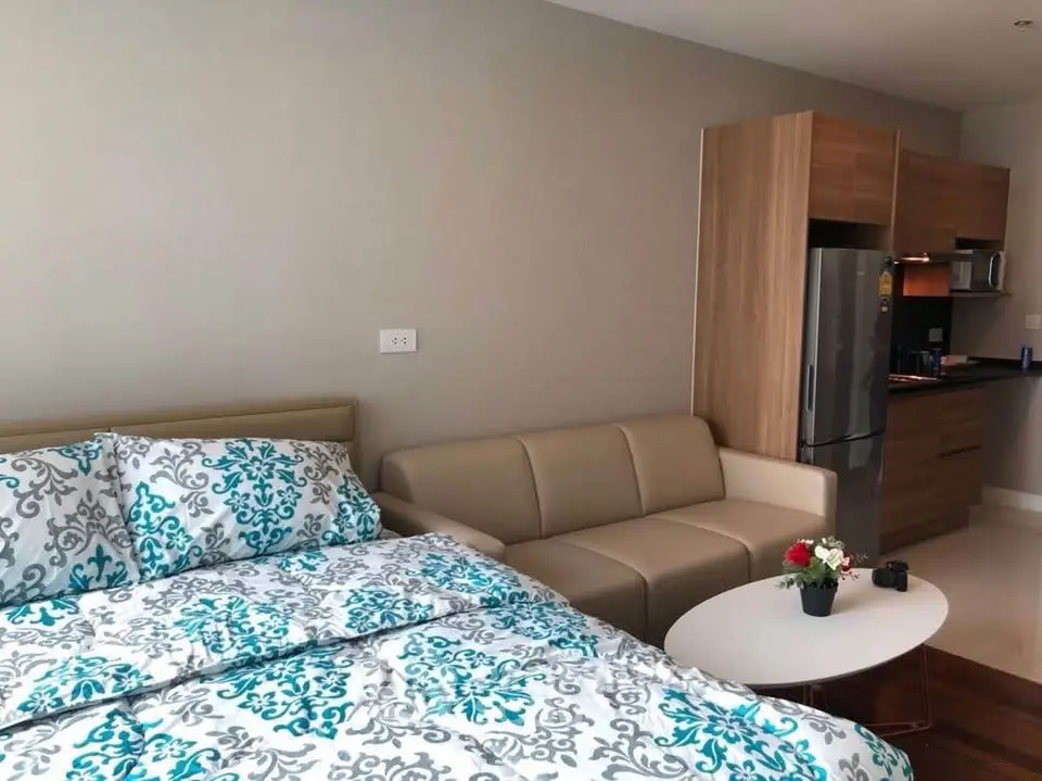 Modern studio apartment with cozy bed, stylish sofa, and compact kitchen area.