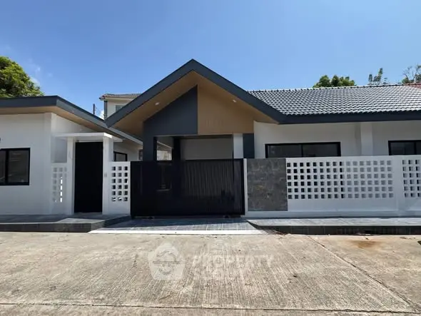 Modern single-story house with sleek design and gated entrance, featuring a contemporary roofline and spacious driveway.