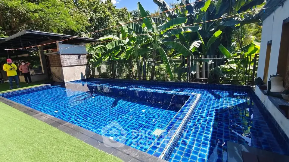 Stunning outdoor pool with vibrant blue tiles surrounded by lush greenery, perfect for relaxation.