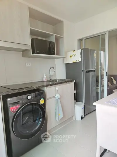 Modern kitchen with washing machine, microwave, and fridge in a compact open layout.