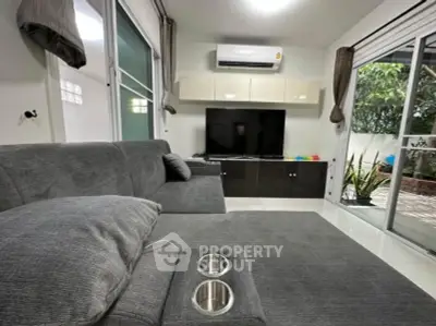 Modern living room with sleek gray sofa and large TV, featuring a cozy ambiance and garden view.