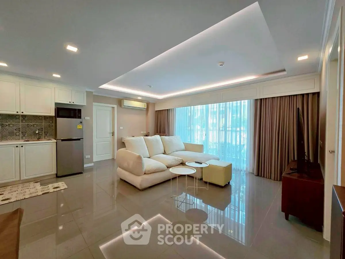 Spacious modern living room with open kitchen, featuring sleek furniture and large windows for natural light.