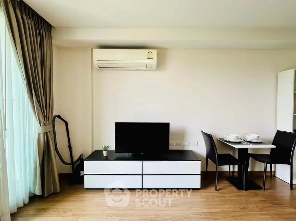 Modern living room with sleek furniture and natural light, featuring a TV and dining area.