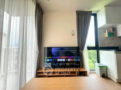 Modern living room with large TV and natural light from balcony, perfect for relaxation.