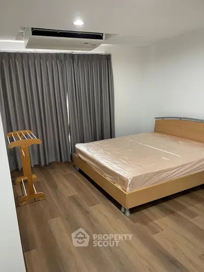 Spacious bedroom with modern wooden flooring and large window curtains