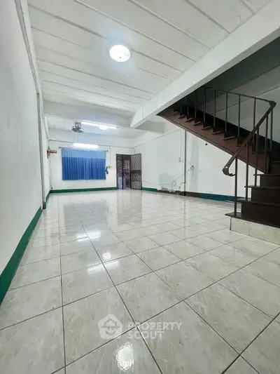 Spacious open-plan living area with tiled flooring and staircase, ideal for customization.