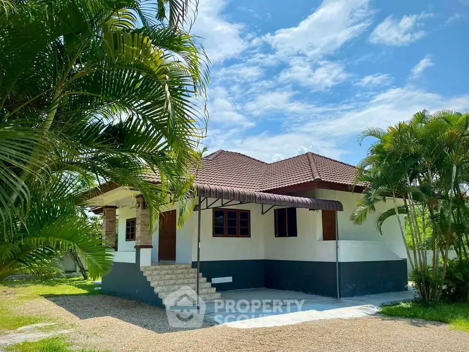 Charming single-story house with lush greenery and spacious driveway under a clear blue sky.