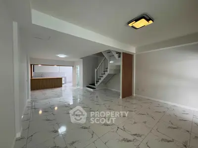 Spacious open-plan living area with modern staircase and sleek tiled flooring.