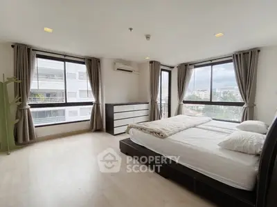 Spacious bedroom with large windows and modern furnishings in a high-rise apartment.