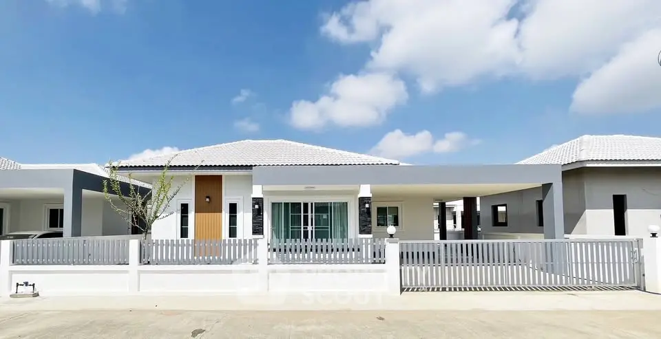 Modern single-story house with white facade and spacious driveway under blue sky.