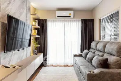 Modern living room with plush sofa, wall-mounted TV, and large window with curtains.