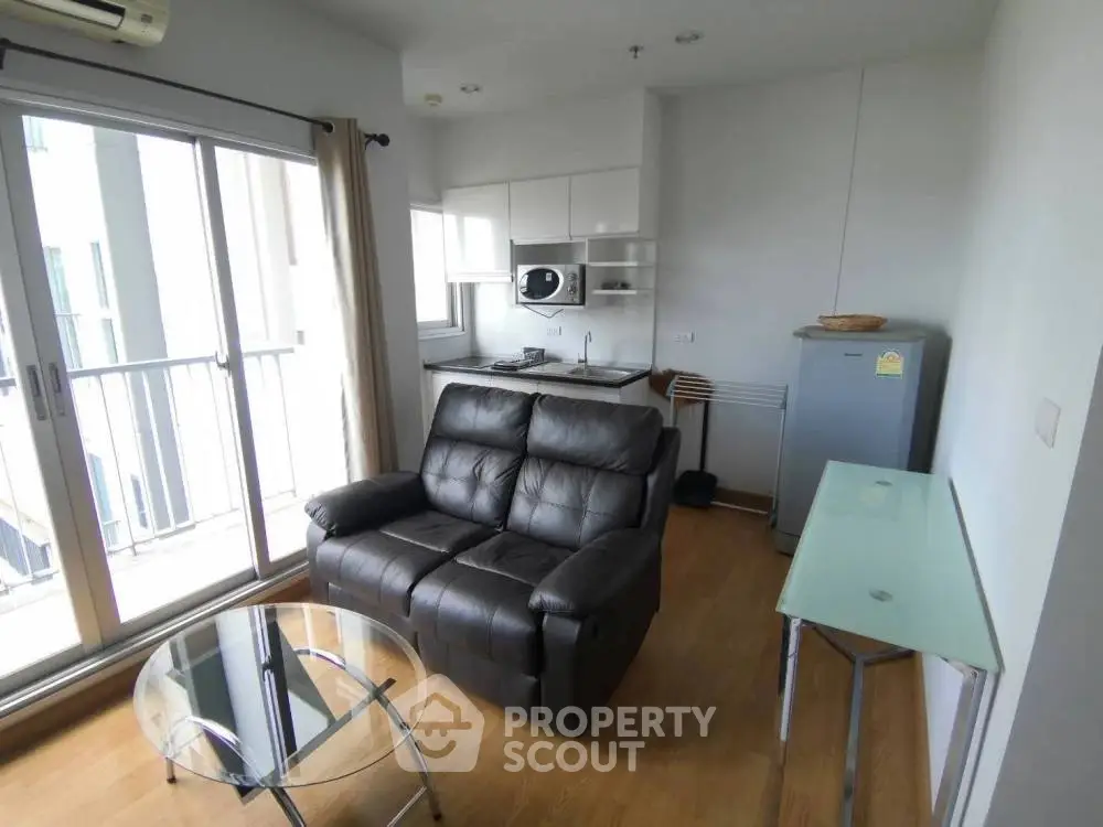 Modern living room with balcony access, featuring sleek furniture and a compact kitchen area.