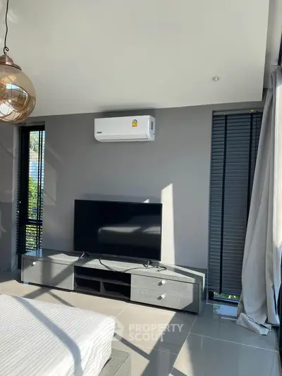 Modern living room with sleek TV setup and air conditioning, featuring stylish blinds and natural light.