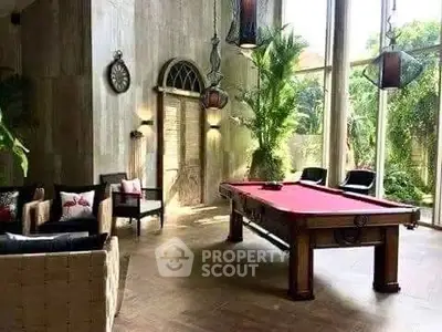 Luxurious living room with pool table and tall windows offering lush garden views.