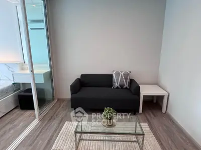 Modern living room with sleek black sofa, glass coffee table, and cozy decor in a stylish apartment.
