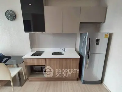 Modern compact kitchen with sleek cabinets and stainless steel fridge in a stylish apartment.