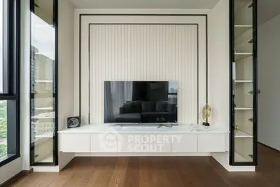 Modern living room with sleek TV unit and large windows offering city views.