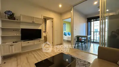 Modern living room with TV and glass doors leading to dining area in stylish apartment.