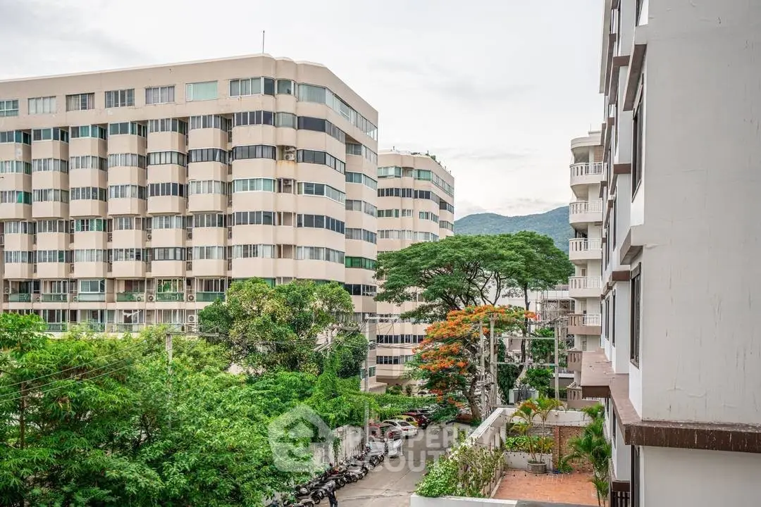 Scenic view of modern apartment buildings with lush greenery and mountain backdrop.