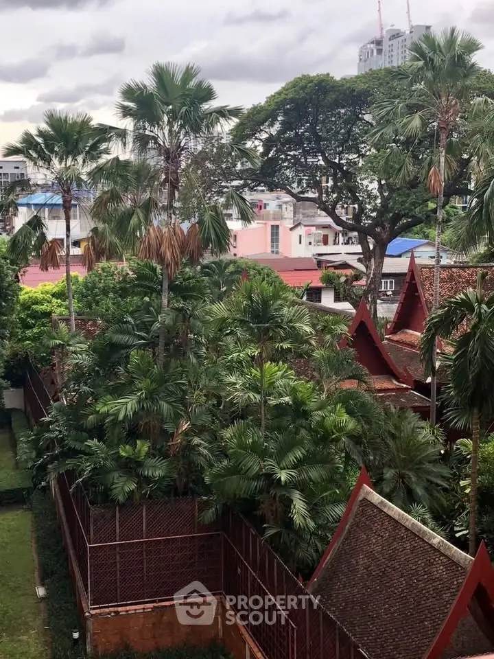 Lush garden view with tropical trees and traditional architecture in urban setting.