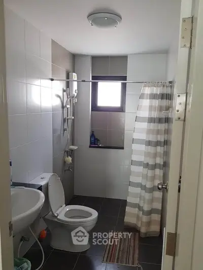 Modern bathroom with shower and window, featuring sleek tiles and a striped shower curtain.