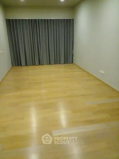 Spacious empty room with wooden flooring and large window with curtains