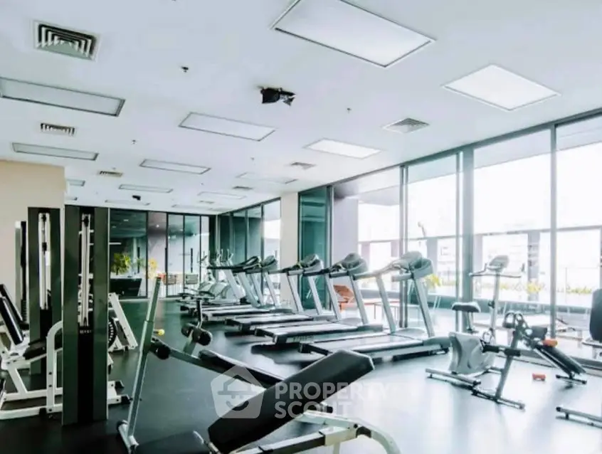 Spacious modern gym with state-of-the-art equipment and large windows offering natural light.