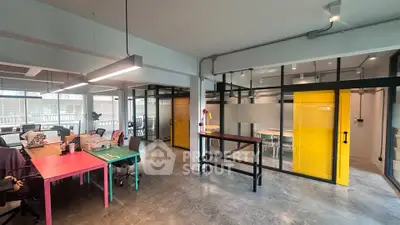 Modern office space with colorful desks and glass partitions, ideal for creative work environments.