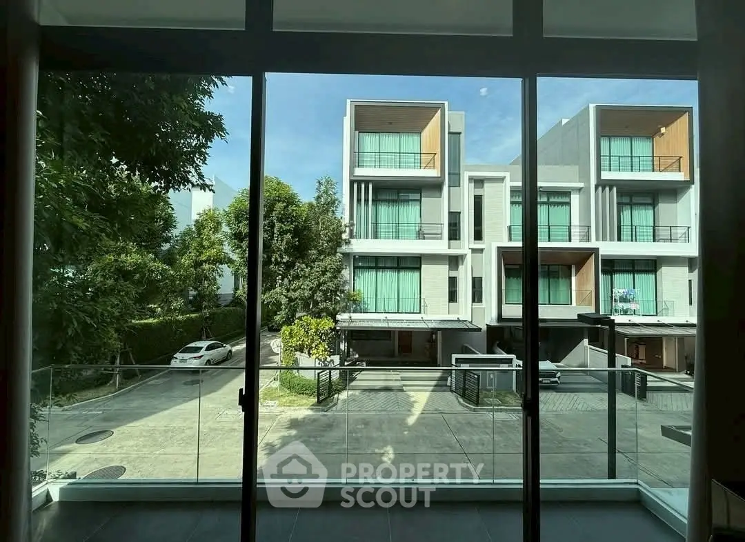 Modern townhouse view from balcony with large glass doors and lush greenery.