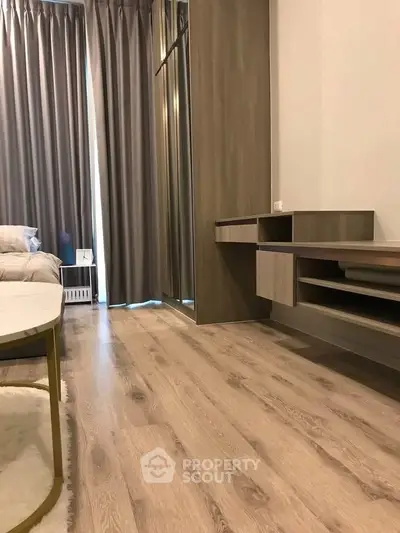 Modern bedroom with wooden flooring and stylish furniture, featuring a cozy bed and elegant curtains.