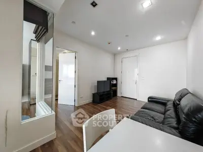 Modern living room with sleek leather sofa and wooden flooring, featuring a minimalist design and ample lighting.