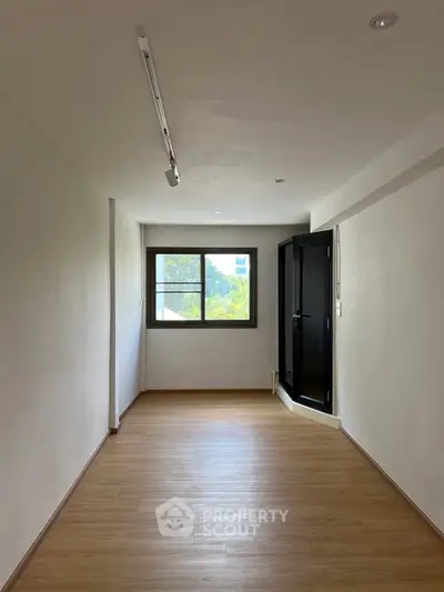 Spacious empty room with wooden flooring and large window, perfect for customization.