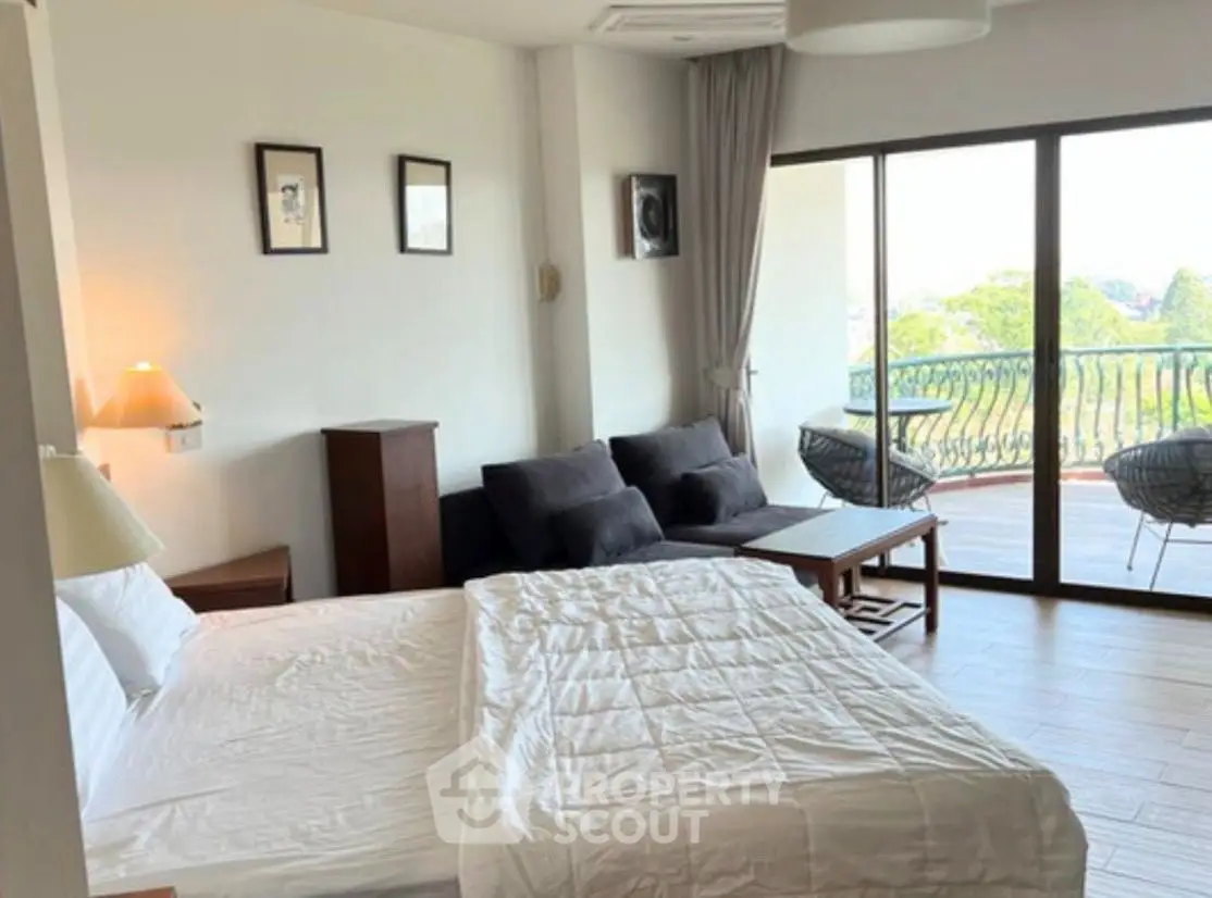 Spacious bedroom with balcony offering scenic views and cozy seating area.